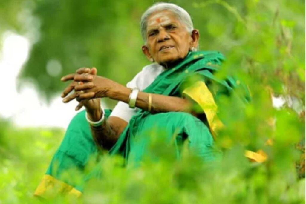 सालुमरदा तिम्मक्का हरे रंग की साड़ी में हरे घास के बीच बैठी हैं और अपने हाथों को जोड़कर देख रही हैं।